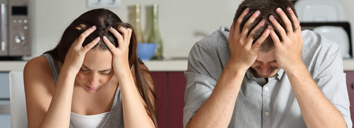 bad tenant Front view of a sad couple with hands on head sitting in the kitchen of a house