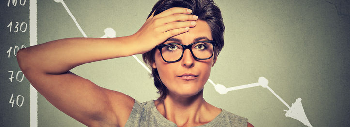 Stressed shocked woman in glasses with financial market chart graphic going down on grey office wall background. Poor economy concept. Face expression, emotion, reaction