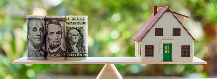 Home loan / reverse mortgage or transforming assets into cash concept : House model, US dollar notes on a simple balance scale, depicts a homeowner or a borrower turns properties / residence into cash