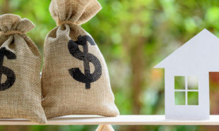 Home loan / reverse mortgage or transforming assets into cash concept : House paper model , US dollar hessian bags on a wood balance scale, depicts a homeowner or a borrower turns properties into cash