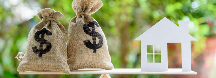 Home loan / reverse mortgage or transforming assets into cash concept : House paper model , US dollar hessian bags on a wood balance scale, depicts a homeowner or a borrower turns properties into cash