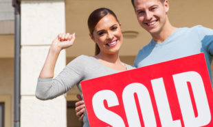 couple holding sold sign in front of their old house