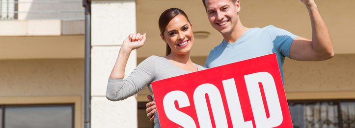 couple holding sold sign in front of their old house