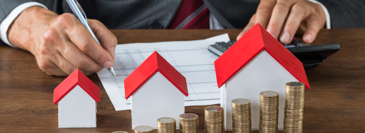 Businessman Calculating Tax By House Models And Coins