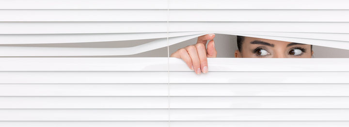 Portrait of a woman looking through out the blinds.