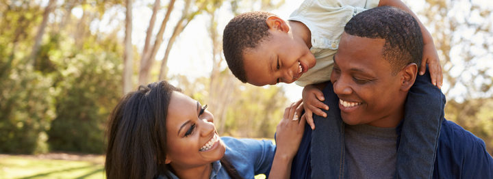 Parents Carrying Son On Shoulders As They Walk In Park