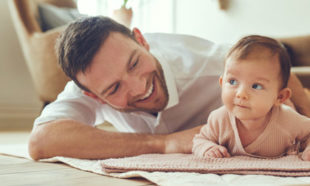 Smiling father lying with his infant daughter at home