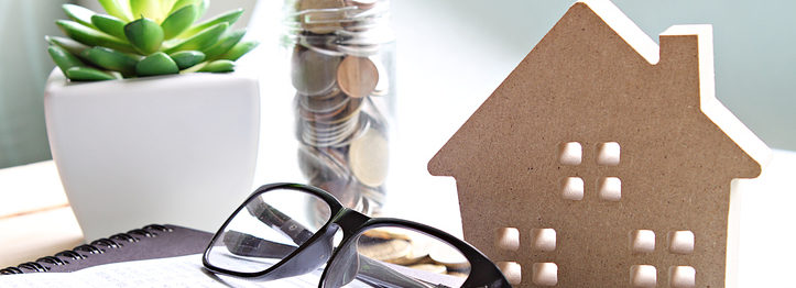 Wood house model, coins, eyeglasses and saving account book or financial statement on office desk table