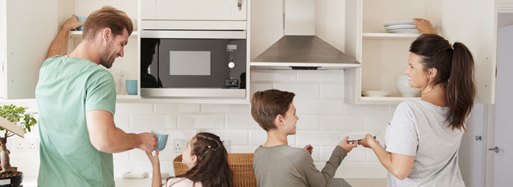 Children Helping To Put Away Crockery In Kitchen Cupboards