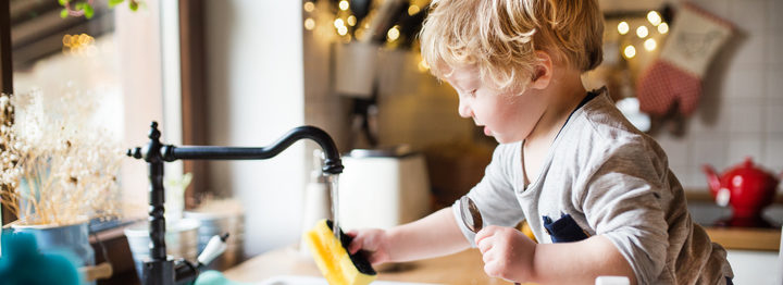 A toddler boy washing up the dishes.