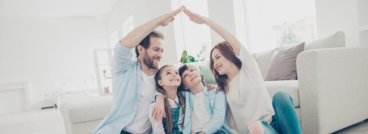 New building residential house purchase apartment concept. Stylish full family with two kids sitting on carpet, mom and dad making roof figure with hands arms over heads